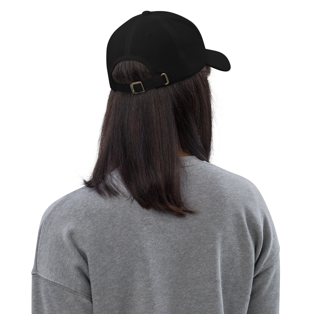 Back view of a black unstructured dad hat with adjustable buckle strap and curved visor worn by person with long hair.
